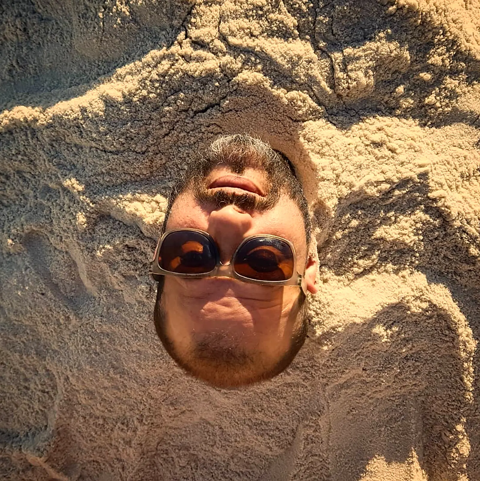 O fundador da High Level em um autorretrato criativo, o rosto emoldurado pela areia da praia, de óculos escuros